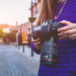 Stylish casual traveler photographer woman taking pictures with digital dslr camera and slr lens during walking around european city