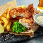 British Traditional Fish and chips with mashed peas, tartar sauce on crumpled paper with cold beer.